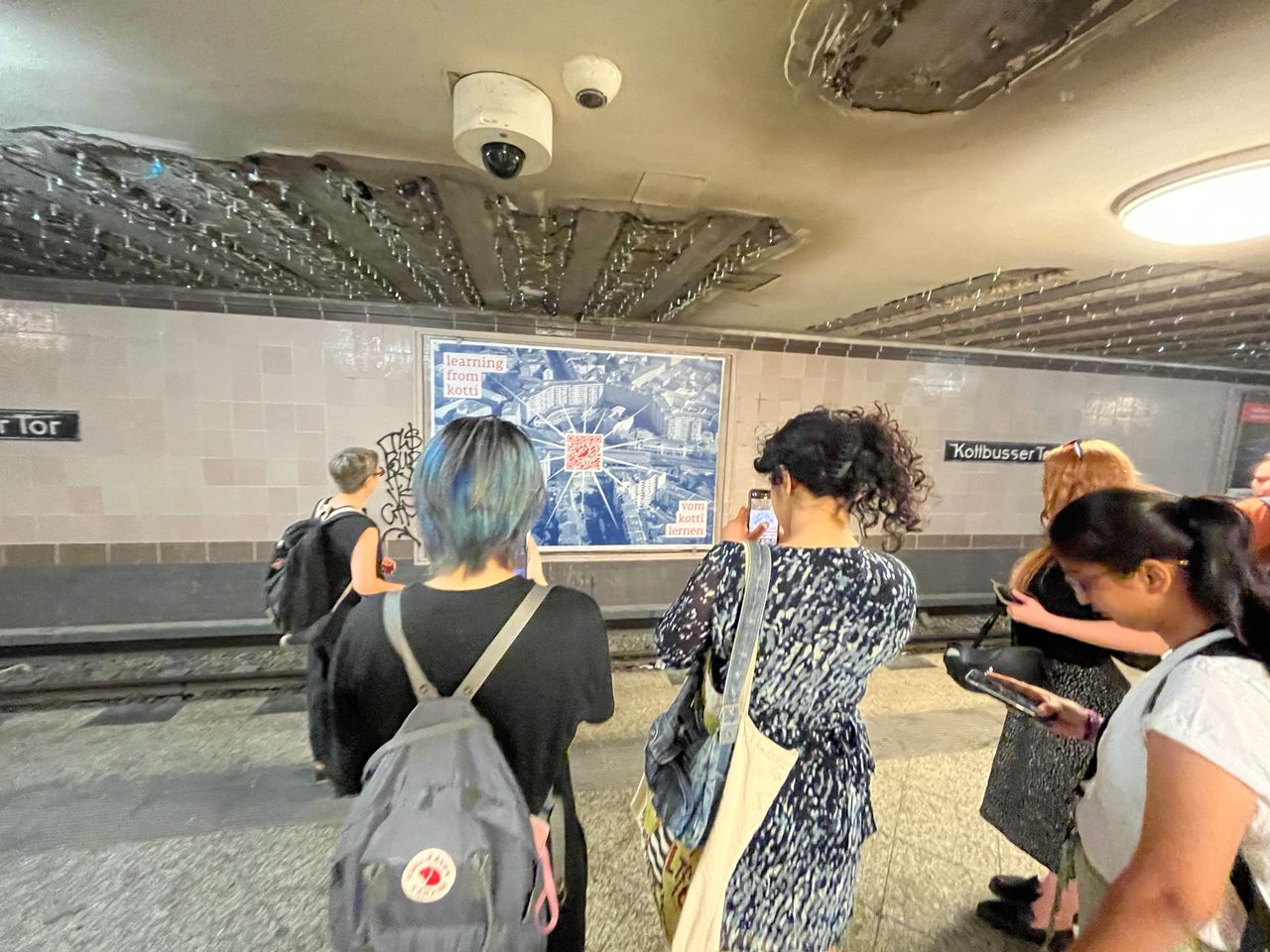 People at Kottbusser Tor station, scanning the QR code from a billboard behind the rails